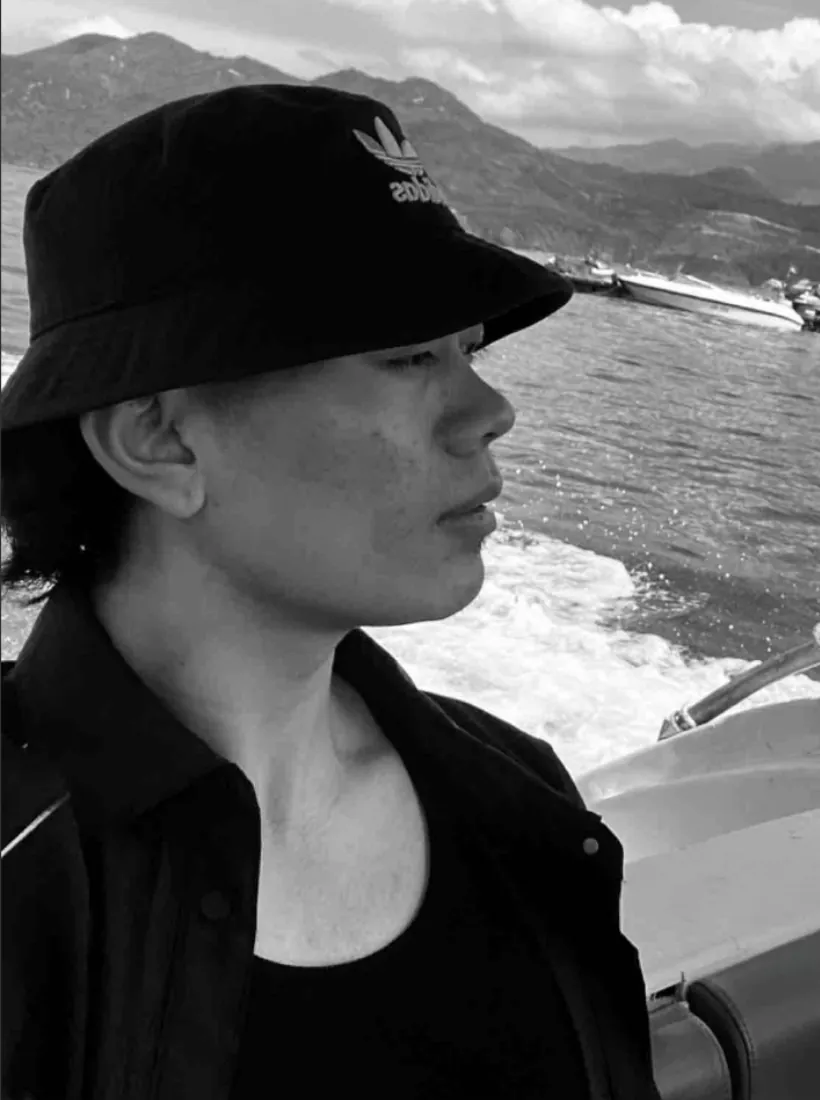 Black-and-white portrait of Lobsang Soepa in a bucket hat, on a boat with mountains behind
